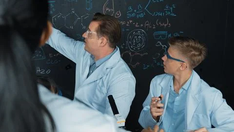 Creative teacher pointing at blackboard while talking to smart boy. Edification. Stock Photos
