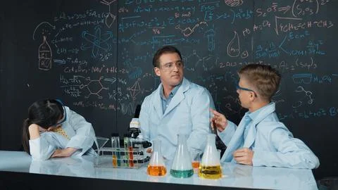 Creative teacher pointing at blackboard while talking to smart boy. Edification. Stock Photos