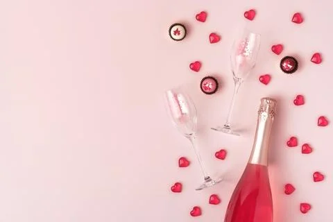 Creative trendy flat lay with pink champagne bottle and flutes, red glass hearts Stock Photos
