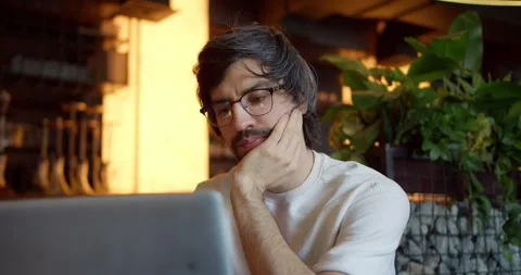 Creative Vibes: Brunette Guy in Glasses Working on Laptop at a Sunny Cafe-Bar Stock Footage 242899850
