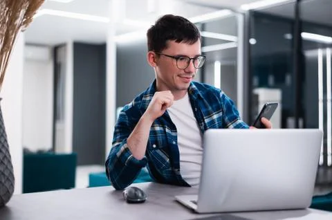 Creative worker. Cheerful young man using his mobile phone while sitting at his Stock Photos