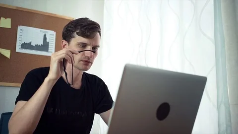Creative young man holds in hands glasses, look at the laptop screen. Stock Footage 79897332