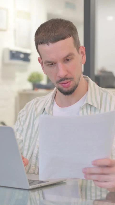 Creative Young Man Working on Documents and Laptop, vertical video 動画素材 325563922