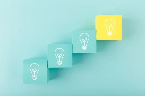 Creativity concept. Light bulbs on blue and yellow toy cubes as a ladder on blue Stock Photos