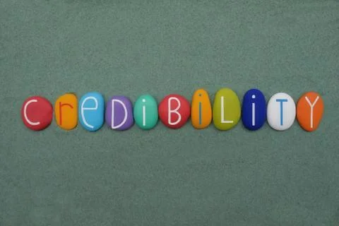 Credibility word composed with multicolored stone letters over green sand Stock Photos