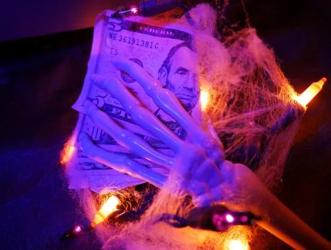 Creepy Skeleton Hand Holding Money Halloween in Cobwebs and Lights Blue Stock Photos