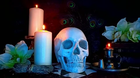 Creepy Skull Under Light Blue Lighting, Candles, Flowers and a Stack of Books Stock Footage 211369268
