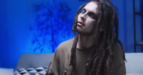 A creepy walking dead with dreadlocks sitting on sofa at the home party. Scary Stock Footage 134940696