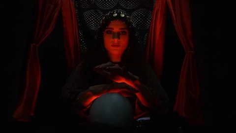 Creepy witch sitting in front of the crystal ball in red light Stock Footage 101370871