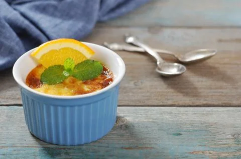 The creme brulee in ceramic baking mold with orange on wooden table Stock Photos