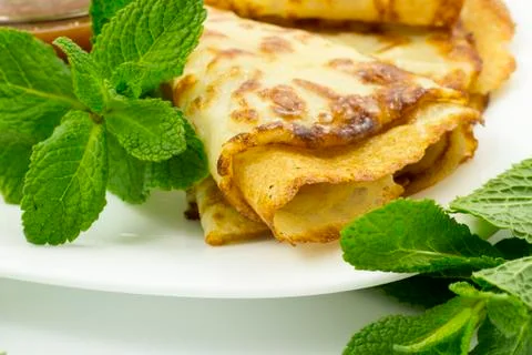 Crepes on a white plate with mint leaves and a Cup of honey Stock Photos