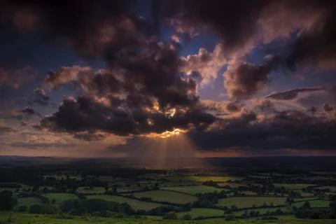 Crepuscular rays of sunlight shine onto fields in Dorset Stock Photos