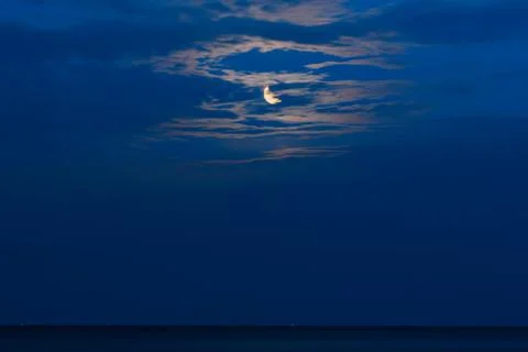 Crescent moon casts a golden reflection across the still water under a deep.. Stock Photos