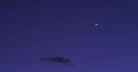Crescent moon in a deep blue evening sky at the cusp of darkness. Fotos Stock