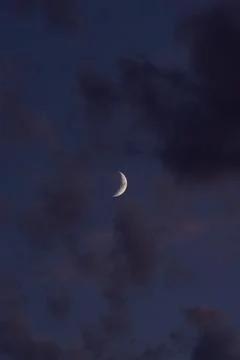 Crescent moon glows softly through deep twilight clouds Fotos Stock