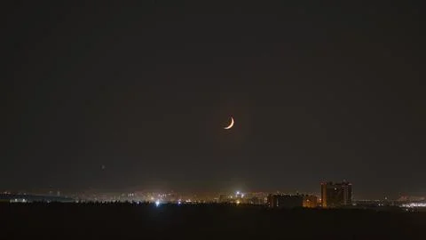 A crescent moon in the night sky is setting over the horizon, timelapse. New Stock Photos