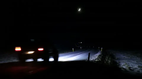 Crescent moon over passing car driving a dark lonely solitary winter night  Stock Footage