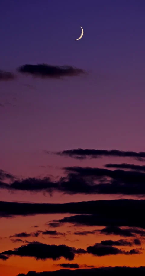 Crescent moon in purple twilight sky with dark clouds at sunset Vídeo Stock 338421346