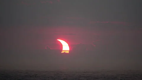 A crescent-shaped partial solar eclipse rises at dawn over the Atlantic Stock Footage 155670150