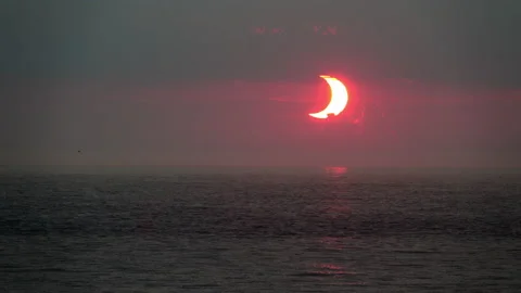 Crescent-shaped sun at dawn, during a partial solar eclipse, rises over Stock Footage 155669639