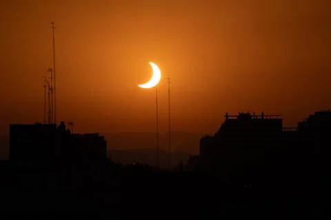 Crescent sun of partial eclipse above city rooftops Stock Photos