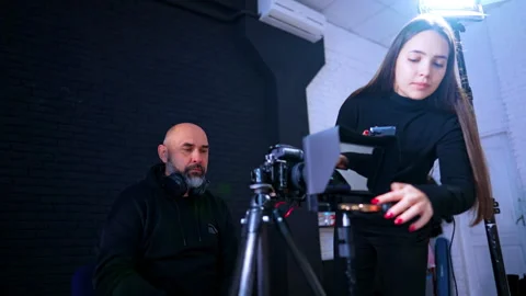 Crew adjusting teleprompter and camera settings in professional studio. Woman Stock Footage 334813077