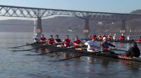 A crew boat team rows with bridge in background Stock Footage