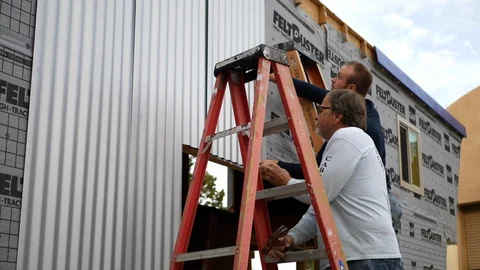 A crew of construction workers installing metal siding on a tiny house job Video stock 120755739