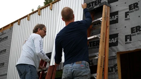 A crew of construction workers measuring and installing metal siding on a Video stock 120755771