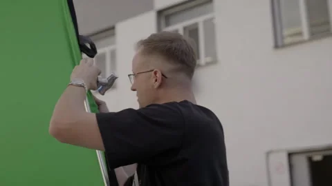 Crew member dependably secures green screen to tripod Vídeos de archivo 306553524