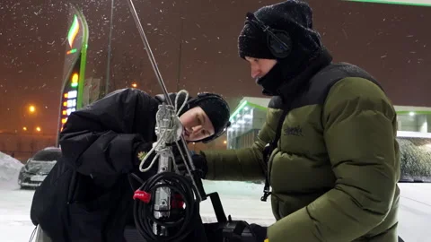Crew members assemble tall camera tripod under snowfall Stock Footage 308940443