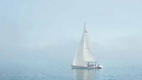 Crew members navigate a white sailboat through dense morning fog on calm water Stock Footage 345118963