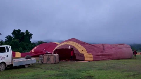 Crew preparing a hot air balloon at dawn in a Vang Vieng field under cloudy Stock Footage 321747676