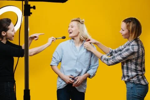 Crew in studio correcting clothes and applying makeup to a model over yellow Stock Photos