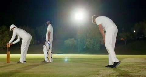 Cricket bowler bowling under floodlights after keeper giving thumbs-up, fielder Stock Footage 345061983