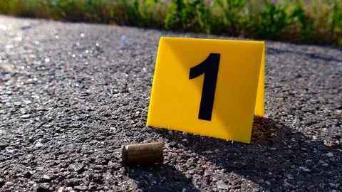 Crime scene evidence marker identifying bullet casing on asphalt Stock Photos