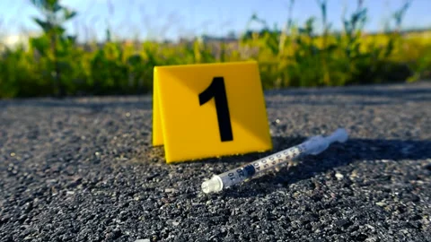 Crime Scene Evidence Marker Next to a Syringe on the Road, Bokeh Background Stock Footage 338993784