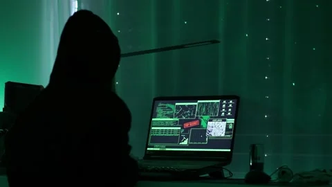 A criminal hackergirl with black hood using laptop and big computers to Stock Footage 152122269