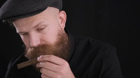 Criminal man in cap sniffs cigar on black background.close up,caucasian Stock Footage 130227450