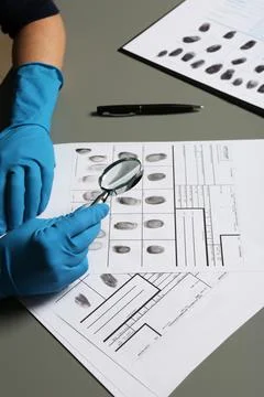 Criminalist exploring fingerprints with magnifying glass at table, closeup Stock Photos