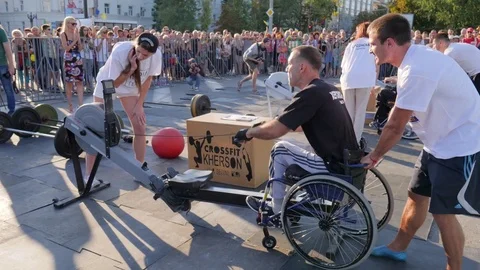 Crippled guy on wheelchair pulls cable at sports training apparatus with Video stock 83431464