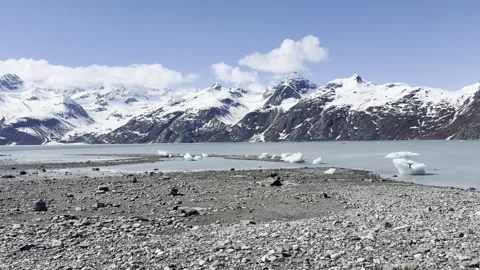 Crisp light catches floating ice across a bay beyond a broad cobble shore Stock Footage 336220213