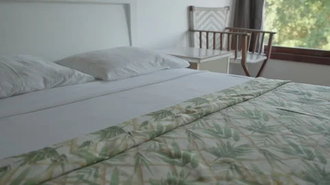 Crisp white bed linen with a leaf patterned throw beside a sunlit window Stock Footage 342863519