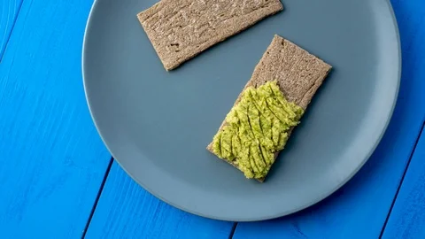 Crispbread with avocado spread are on a blue plate, stop motion top view Stock Footage 126229482