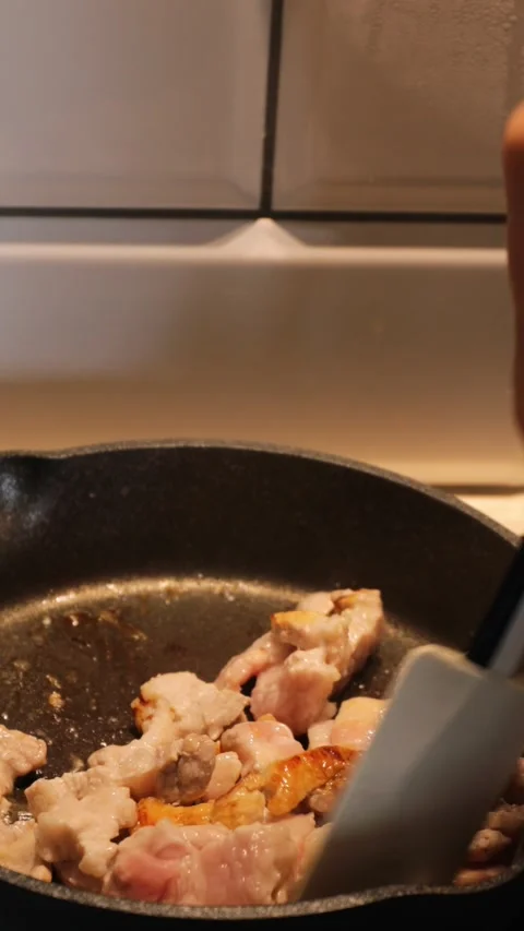 Crispy bacon pieces being flipped with silicone spatula while frying in black Stock Footage 314267093