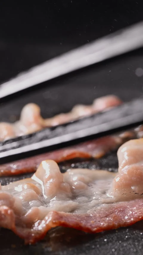 Crispy bacon sizzling in a pan, close-up shot. 動画素材 317453257