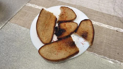 Crispy burnt bread slices on white plate with seasoning on beige tablecloth 库存照片