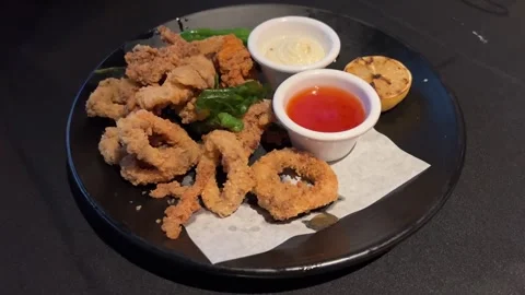 Crispy calamari appetizer with red &amp; white dipping sauce on a black plate 스톡 동영상 329945596