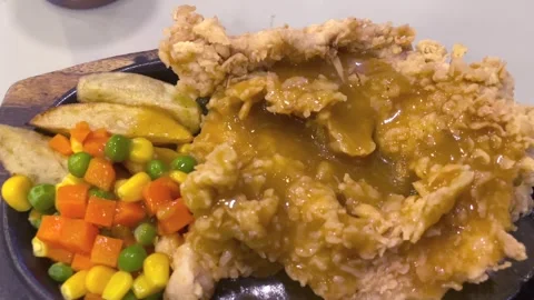 Crispy chicken steak served with brown sauce and mix vegetables on a hot plate Stock Footage 327229088