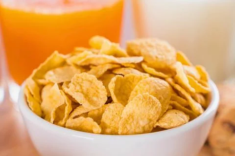 Crispy corn flakes cereal in a white bowl with orange juice and milk Stock Photos